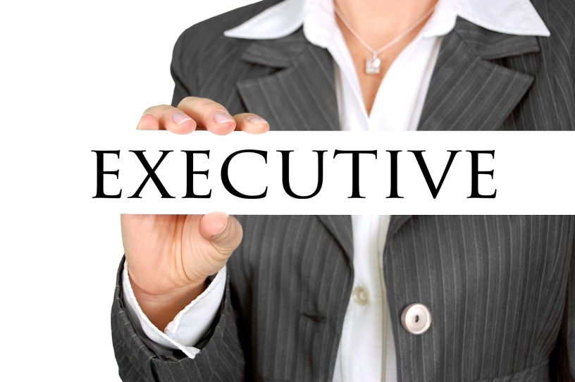A woman's torso is in partial view so you can see her hand holding the word "executive" in capital letters.